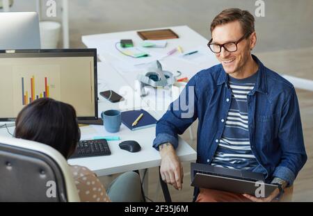 High angle portrait of smiling contemporary businessman talking to African-American colleague while brainstorming project ideas in office Stock Photo