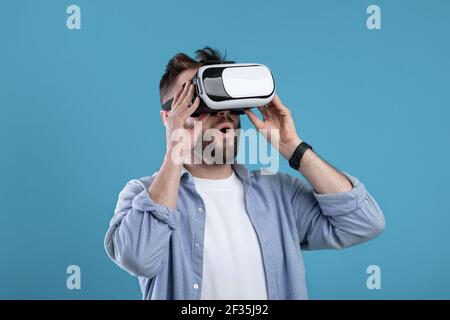 Cool millennial guy experiencing virtual reality in VR headset on blue studio background Stock Photo