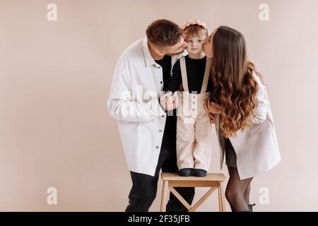 Portrait of a happy young family, with a little adorable daughter. Caring parents holding a baby's hands. mom and dad kissing their child girl on beig Stock Photo