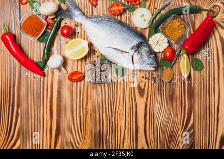 Fresh raw dorado fish on baking paper with lemon, pepper, tomatoes and various spices on wooden background with copy space. Stock Photo