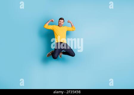 Full body portrait of astonished person jump high fists up open mouth shout yes isolated on blue color background Stock Photo