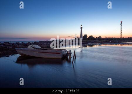 Moon lit seascape view with the fishing boat in front and historic lighthouse and maritime radar tower in background during the light Nordic midsummer Stock Photo