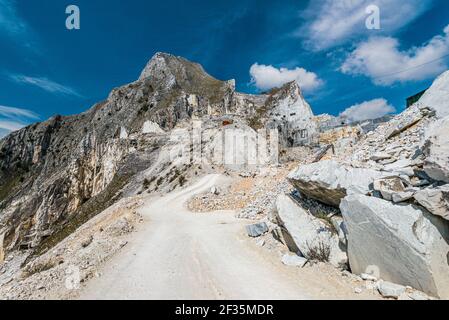 Sunny day on visiting Carrara marble quarry site. Dirt road inside areal. Construction and mining raw material concept. Stock Photo