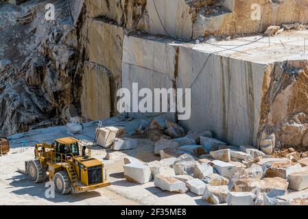 Big yellow front loader standing at huge rock blocks in Carrara marble quarry. Construction and mining raw material concept. Stock Photo