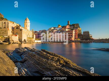 View over big stones on shore at small coastal village built on sharp cliff. Various color buildings over sea water. Cinque Terre, Liguria, Italy. Stock Photo