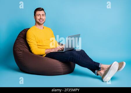 Portrait of attractive cheerful guy sitting in bag chair typing writing email isolated over bright blue color background Stock Photo