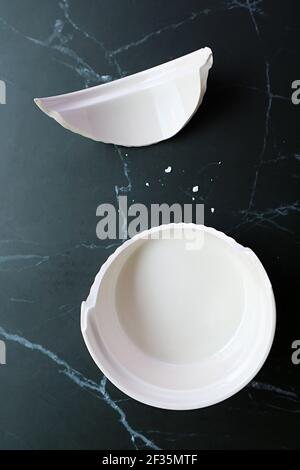 Broken white ceramic baking bowl with fragments on black kitchen countertop Stock Photo