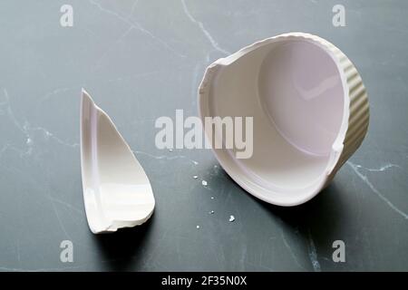 Closeup of broken white ceramic baking bowl with fragments on black marble floor Stock Photo