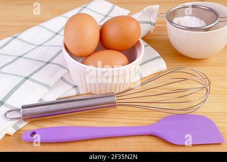 Eggs with a whisk and kitchen utensils on wooden table for home-cooking Stock Photo