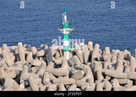 Dolosse type heavy precast concrete blocks in large heap as  breakwater protects green navigation channel marker tower aid & warn shipping Dubai UAE Stock Photo