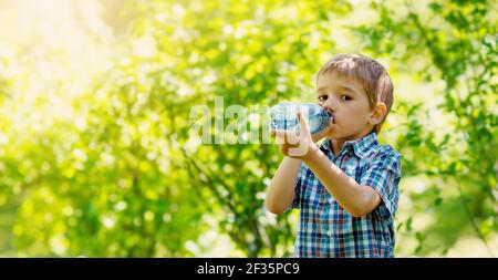 Cute boy drinking a bottle of pure water in nature. Stock Photo