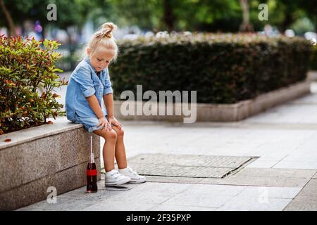 Cute Stylish little girl with blonde hair drinking soda outdoor at hot summer day, Unhealthy drink for Children Stock Photo