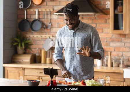 Young african guy broadcast live preparing dish on domestic kitchen Stock Photo