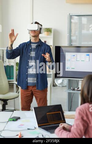 Vertical portrait of IT development team designing immersive reality software with focus on man wearing VR headset in office Stock Photo