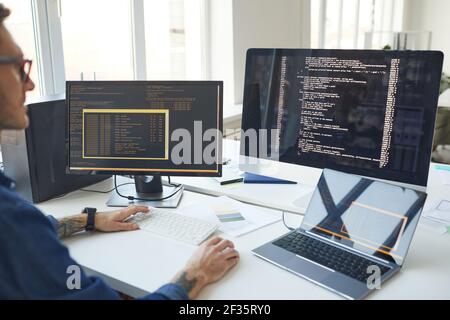 Side view at male programmer writing code while using multiple computers in IT developers office , copy space Stock Photo
