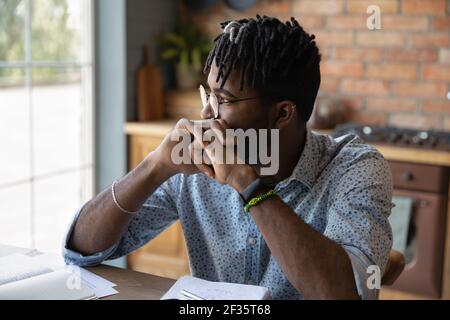 Pensive african male student sit at table reflect on task Stock Photo