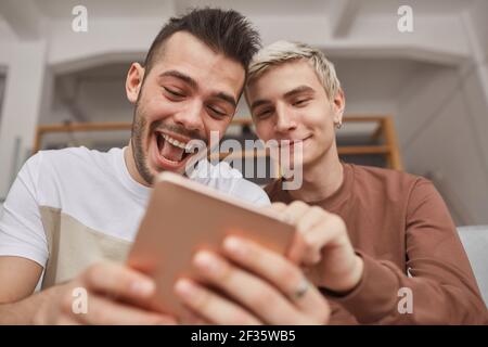 Low angle portrait of two young men laughing while looking at tablet screen in home interior Stock Photo