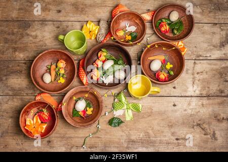 Easter ceramic bowls with eggs, bunnies, and fresh roses on a vintage table. Collection of traditional dishes with fresh flowers, cups, and ribbons. F Stock Photo