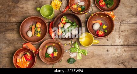 Easter ceramic bowls with eggs, bunnies, and fresh roses on a vintage table. Collection of traditional dishes with fresh flowers, cups, and ribbons. F Stock Photo