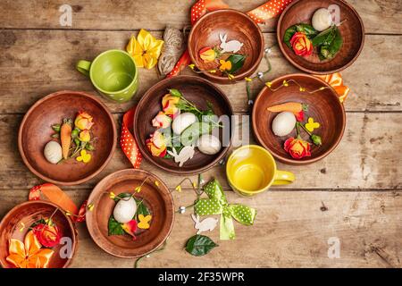 Easter ceramic bowls with eggs, bunnies, and fresh roses on a vintage table. Collection of traditional dishes with fresh flowers, cups, and ribbons. F Stock Photo