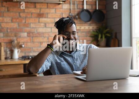 Positive african man answer phone call reading data on laptop Stock Photo