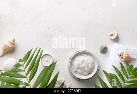 spa border with natural sea salt in a bowl, candles, shells and green palm leaves on a white stone background. Relaxation and zen like concept. top Stock Photo