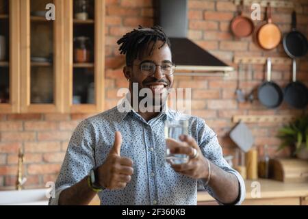 Casual guy holding a glass of water and giving thumb up isolated on ...