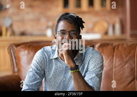 Smiling young black male sitting on sofa looking at camera Stock Photo