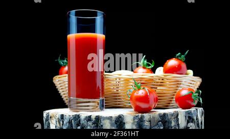 Tomato juice with tomatoes on a wooden board on a black background. Fresh tomatoes in a basket with freshly squeezed tomato juice. Stock Photo