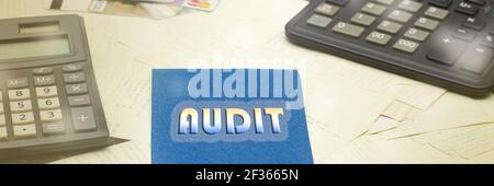 AUDIT text on a blue piece of paper on a writing desk, next to black calculators and a lot of checks Stock Photo