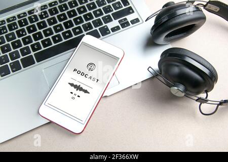 Smartphone playing a podcast. Mobile phone, laptop and headphones on white background. Concept of listening to podcast Stock Photo