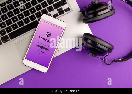 Smartphone playing a podcast. Mobile phone, laptop and headphones on violet background. Concept of listening to podcast Stock Photo