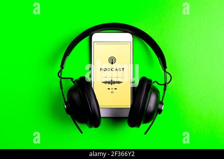 Smartphone playing a podcast. Mobile phone and headphones on green background. Concept of listening to podcast Stock Photo