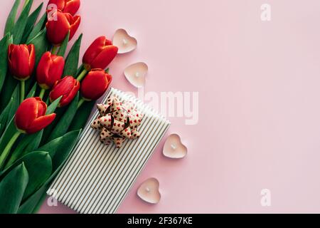 Pink background with place for text with red fresh flowers tulips gift box and heart shaped candles. Stock Photo