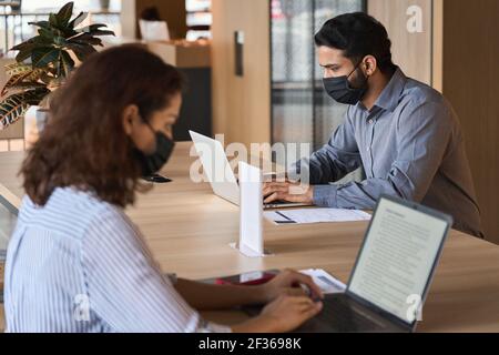 Diverse people wearing face masks working on laptops keeping safe distance. Stock Photo