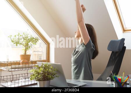 Woman stretching her hands up at office desk in a break from work at home office. Exercise and healthy living concept. Stock Photo