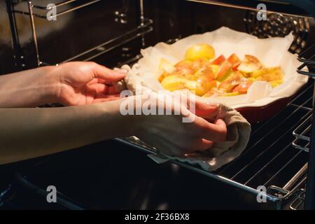 The hostess prepares apple charlotte at home in the kitchen and puts in the oven an apple pie Stock Photo