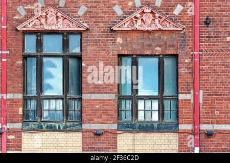 Two rectangular windows with a triangular canopy and pink stucco on the background of an old red brick wall. From the windows of the world series. Stock Photo