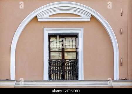 Rectangular window with a French balcony on a pink wall framed by white stucco moldings in the form of an arch. From a series of windows of St. Peters Stock Photo
