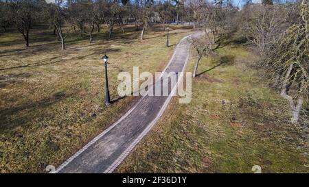 Flight over the city park. A pedestrian alley is visible below. High-rise city houses in the distance. Stock Photo