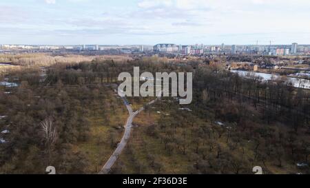 Flight over the city park. A pedestrian alley is visible below. High-rise city houses in the distance. Stock Photo