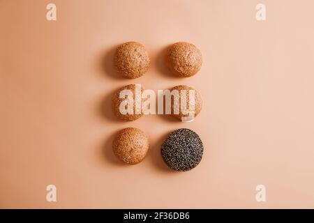 Traditional and one black cuttlefish ink burger buns with sesame seeds without adding arranged in two rows, isolated on beige background. Homemade ham Stock Photo