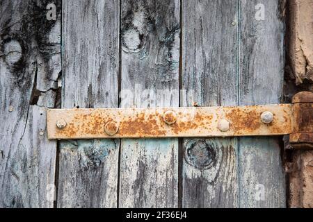 Old rusty hinge on an old wooden door painted blue. Detail of the different textures of the metal and wood. Stock Photo