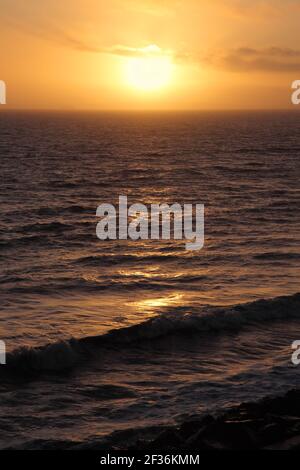 Sea and waves to to the horizon with yellow orange sunset or setting sun low in the sky Stock Photo