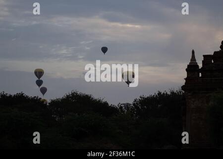 BAGAN, NYAUNG-U, MYANMAR - 2 JANUARY 2020: A few hot air balloons in the sky during early morning on a cloudy day over a temple