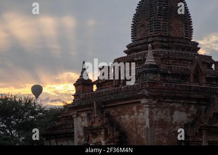 BAGAN, NYAUNG-U, MYANMAR - 2 JANUARY 2020: A hot air balloon rises behind a historic pagoda temple during early morning sunrise Stock Photo