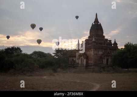 BAGAN, NYAUNG-U, MYANMAR - 2 JANUARY 2020: A few hot air balloons rises behind a historic pagoda temple during early morning sunrise Stock Photo