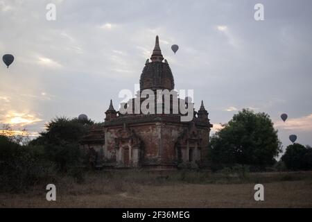 BAGAN, NYAUNG-U, MYANMAR - 2 JANUARY 2020: A few hot air balloons rises behind a historic pagoda temple during early morning sunrise Stock Photo