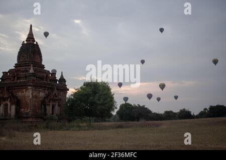 BAGAN, NYAUNG-U, MYANMAR - 2 JANUARY 2020: A few hot air balloons rises behind a historic pagoda temple during early morning sunrise Stock Photo