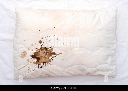 Old used white pillow with stains on crumpled sheet, dirty pillow on the bed Stock Photo